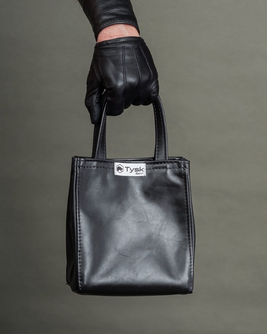 Black leather bag with a short handle and the Tysk logo