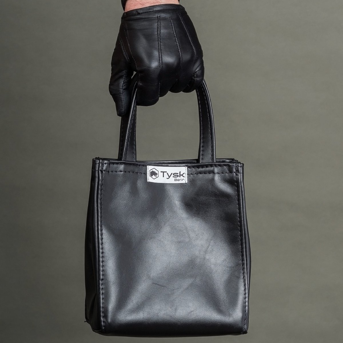 Black leather bag with a short handle and the Tysk logo